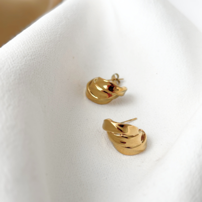 Brincos dourados com design torcido sobre tecido branco