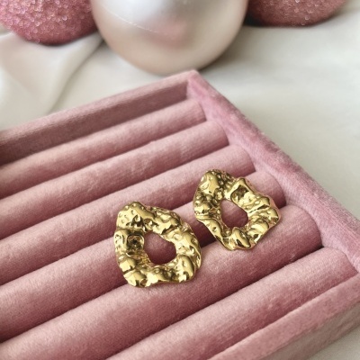 Brincos dourados texturizados em caixa rosa com bolas decorativas ao fundo