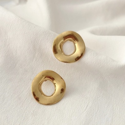 Brincos dourados com forma irregular sobre tecido branco