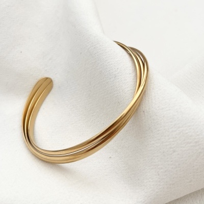 Pulseira dourada de três fios entrelaçados sobre tecido branco