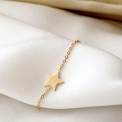 Pulseira dourada com pendente estrela sobre tecido branco