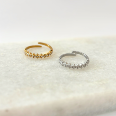 Dois anéis ajustáveis, dourado e prateado, com pedras brilhantes e relevo, sobre superfície marmorizada clara