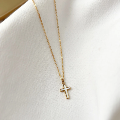 Colar dourado com pendente cruz oca sobre tecido branco