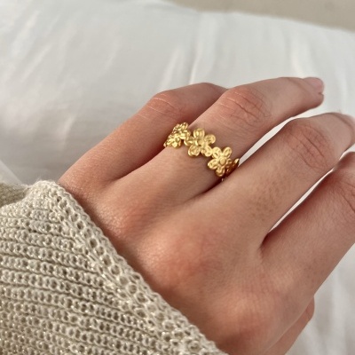 Anel dourado com flores numa mão com camisola creme