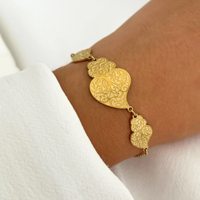 Pulseira dourada com três corações gravados, usada no pulso