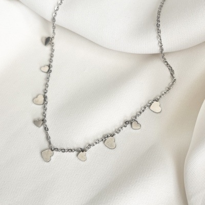 Colar prateado com pendentes em forma de corações sobre tecido branco