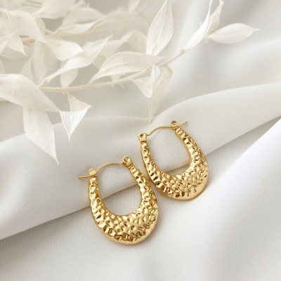 Brincos dourados com textura em tecido branco com folhas secas