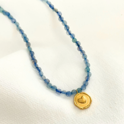 Colar azul com pendente dourado de coração sobre tecido branco