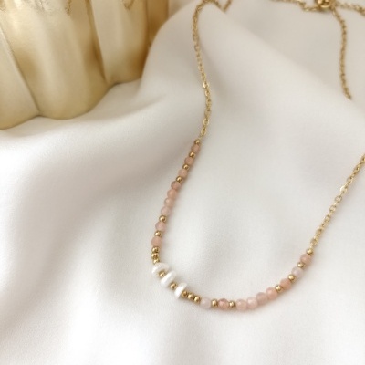 Colar dourado com pérolas e esferas cor de rosa sobre tecido branco