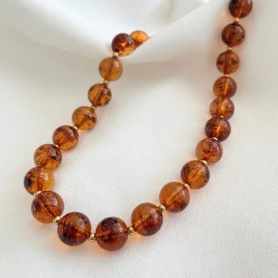 Colar de contas âmbar esféricas com detalhes dourados sobre tecido branco