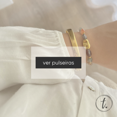 Pulseiras dourada e de pedras coloridas num braço com camisa branca.