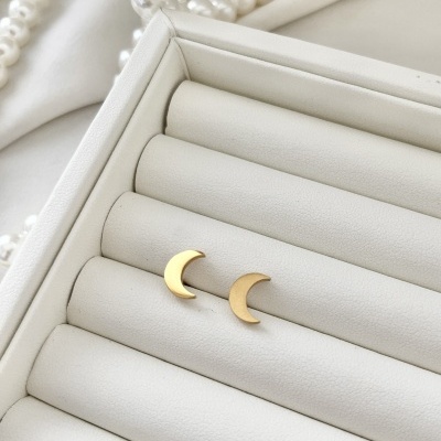 Brincos meia-lua dourados em suporte branco acolchoado com pérolas ao fundo