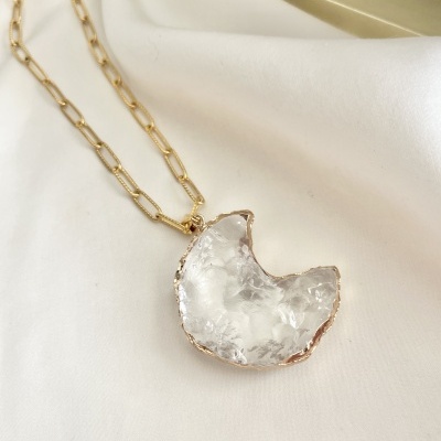 Colar dourado com pendente de pedra transparente irregular sobre tecido branco