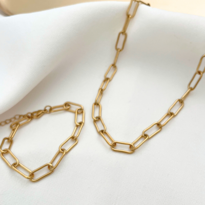 Conjunto de colar e pulseira dourados com elos retangulares sobre tecido branco.