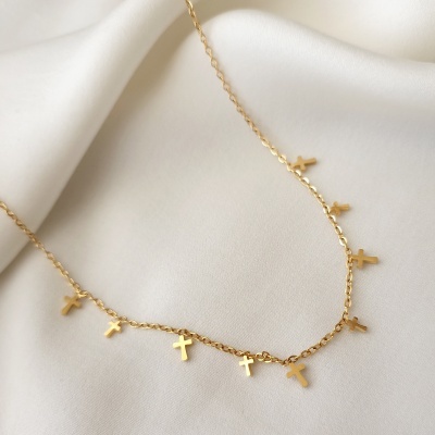 Colar dourado com pendentes de cruz sobre tecido branco
