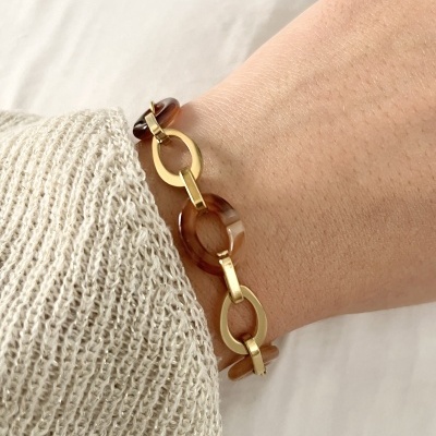 Pulseira elos dourados e resina castanha no pulso com camisola de malha bege