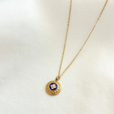 Colar dourado com pendente redondo azul e branco sobre tecido branco