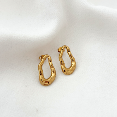 Brincos dourados com design irregular sobre tecido branco.