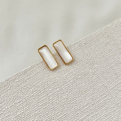 Brincos retangulares dourados com interior branco sobre superfície branca texturada