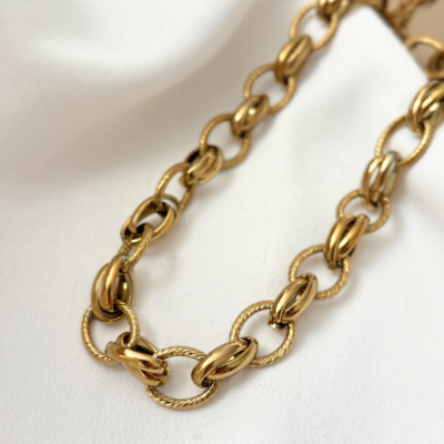 Colar dourado com elos redondos de texturas variadas sobre tecido branco