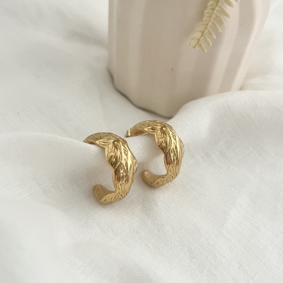 Brincos dourados com textura ondulada sobre tecido branco