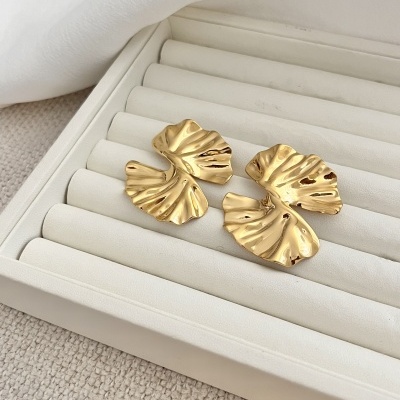 Brincos dourados em forma de folhas numa bandeja de exposição branca acolchoada