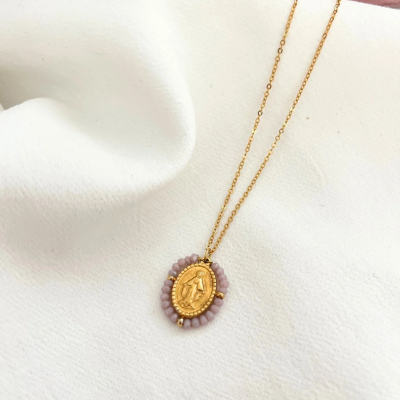 Colar dourado com pendente oval decorado com contas cor-de-rosa sobre tecido branco