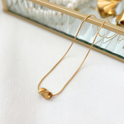 Colar dourado com pendente em forma orgânica em superfície branca e moldura dourada