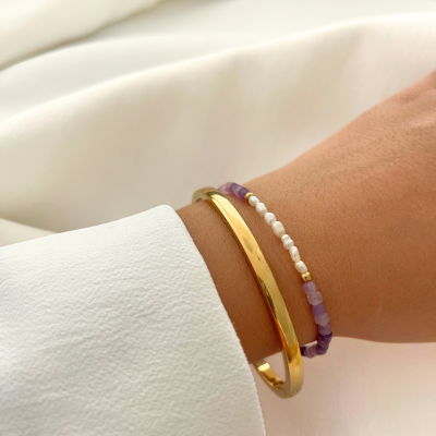 Pulseira de pedras roxas, brancas e douradas e bracelete dourada no pulso com camisa branca
