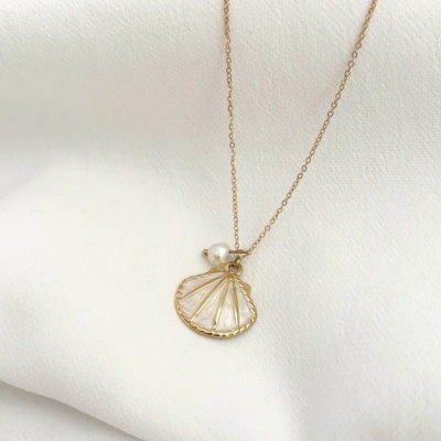 Colar dourado com pendente de concha e pérola sobre tecido branco