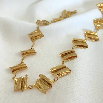 Colar dourado com texturas onduladas sobre tecido branco