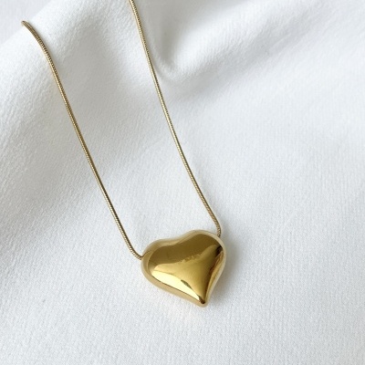 Colar dourado com pendente coração sobre tecido branco