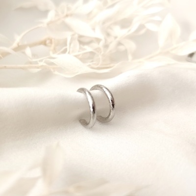 Dois anéis de prata sobre tecido branco com elementos decorativos esbranquiçados