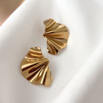 Brincos dourados ondulados sobre tecido branco.