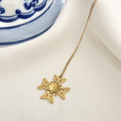 Colar dourado com pendente em forma de estrela, tecido branco e prato azul e branco ao lado