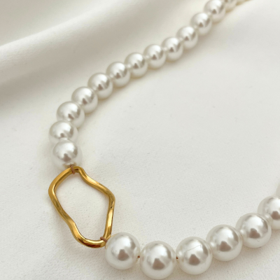 Colar de pérolas brancas com peça em metal dourado sobre tecido branco