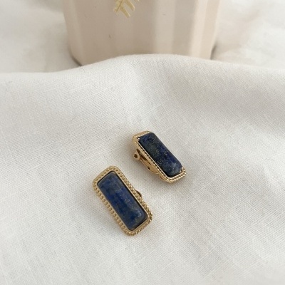 Brincos retangulares com pedras azuis e moldura dourada sobre tecido branco.