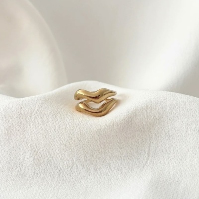 Anel dourado com forma ondulada sobre tecido branco texturizado