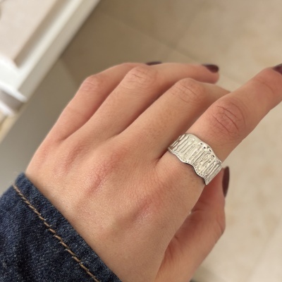 Anel prateado ondulado usado no dedo médio de mão com unhas pintadas