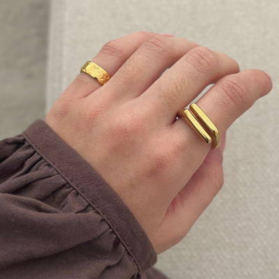 Mão com duas argolas douradas e manga castanha.