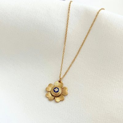 Colar dourado com pendente em forma de flor com centro azul sobre tecido branco
