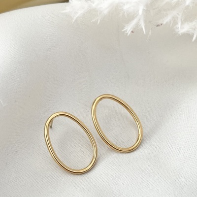 Brincos ovais dourados sobre tecido branco, com pluma branca ao lado.