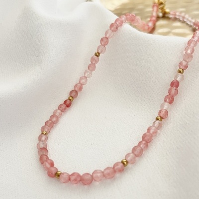 Colar de contas rosa e douradas sobre tecido branco