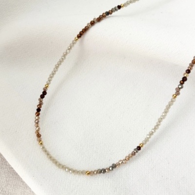 Colar com contas facetadas em tons neutros e dourado sobre tecido branco