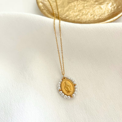 Colar dourado com pendente oval rodeado por pérolas sobre fundo branco e prato dourado