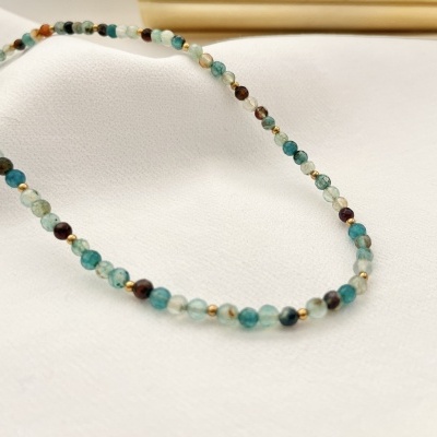Colar de contas azuis, verdes, castanhas e douradas sobre tecido branco