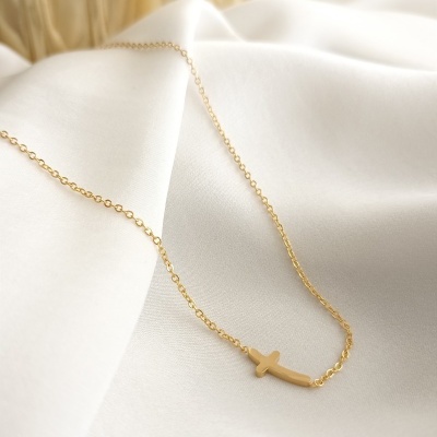 Colar dourado com pendente em forma de cruz horizontal sobre tecido branco