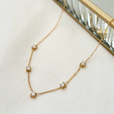 Colar dourado delicado com pedras cristal em fundo branco e espelho dourado