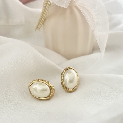 Brincos ovais com pérola falsa e moldura dourada em tecido branco.