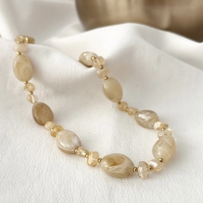 Colar de contas elípticas e transparentes em tons bege e dourado sobre tecido branco